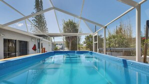 A swimming pool with a glass enclosure, surrounded by a white structure, and trees in the background. - Dockside Hernando Beach Retreat w/ Canal Access (Spring Hill)