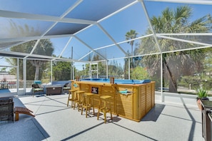 Un espacio al aire libre techado con piscina, taburetes y sillas.