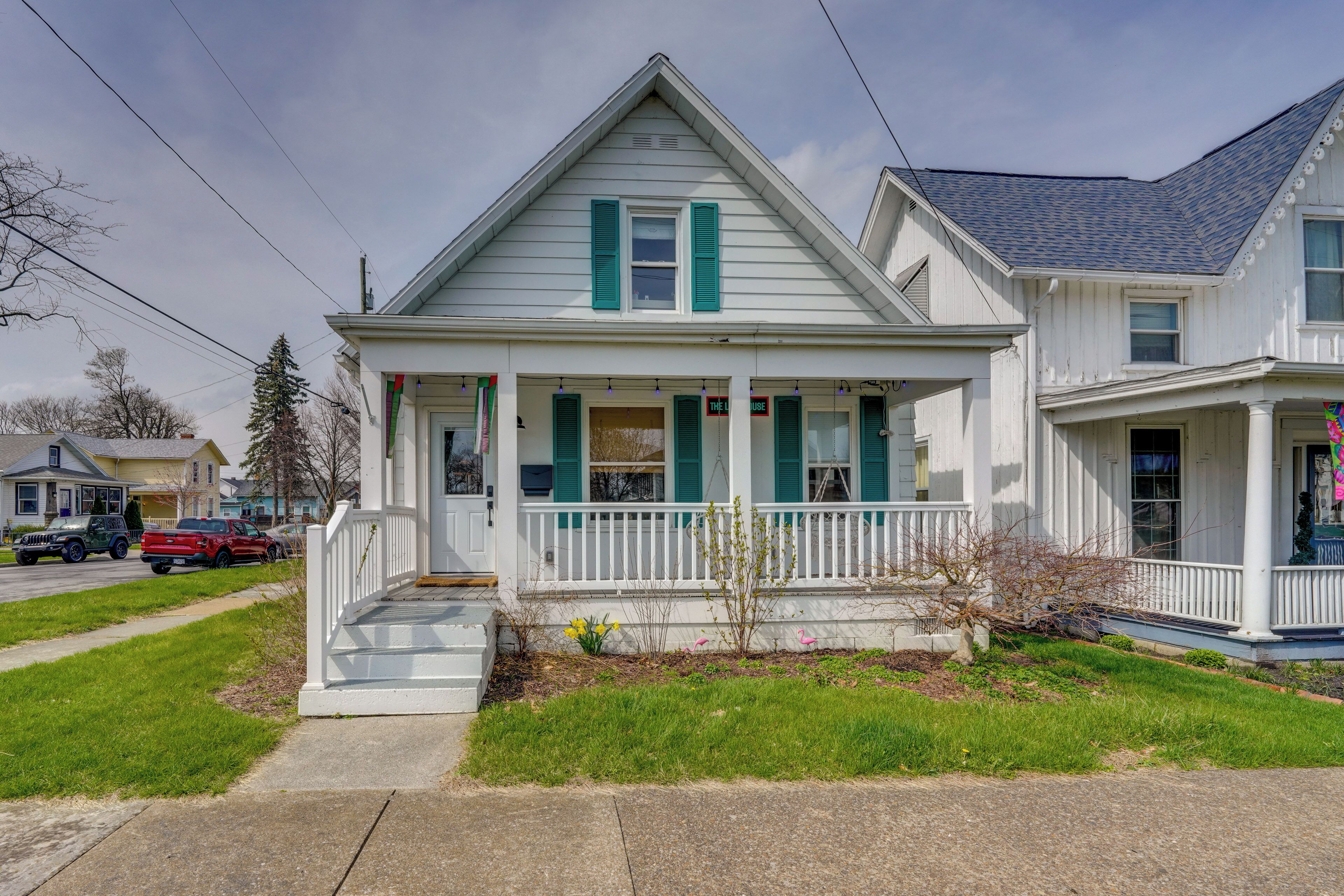 A two-story house with a porch, a small garden, and a street view.
