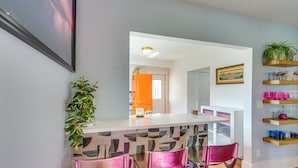 A modern kitchen with a bar area, bar stools, a potted plant, and a view into the dining area. - Explore Dtwn Sandusky! Unique Lake Erie Getaway (Sandusky)