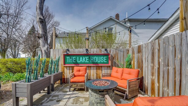 An outdoor patio area with a stone fire pit, orange outdoor furniture, and a wooden fence. - Explore Dtwn Sandusky! Unique Lake Erie Getaway (Sandusky)
