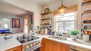 A modern kitchen with a stove, sink, wooden cabinets, and a window with blinds. - Explore Dtwn Sandusky! Unique Lake Erie Getaway (Sandusky)