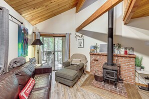 A cozy living room with a fireplace, leather sofa, ottoman, and a large window. - Whitefish Lake Couples Escape w/ Community Perks! (Whitefish)