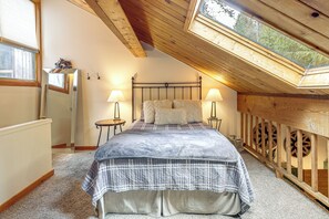 A bedroom with a sloped ceiling, a bed with a quilted bedspread, two bedside lamps, and a small table with a lamp. - Whitefish Lake Couples Escape w/ Community Perks! (Whitefish)