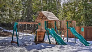 Un parque infantil de madera con dos toboganes y un columpio en un parque nevado.