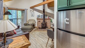 Una sala de estar acogedora con sofá, una mesa con lámpara, chimenea y una cocina con refrigerador de acero inoxidable.