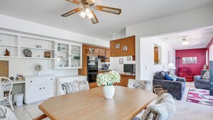 A modern kitchen with white cabinetry, a dining table with chairs, a ceiling fan, and a living area with a sofa and a TV. - On Sun City South Golf Course! Quiet Home w/ Patio (Sun City)