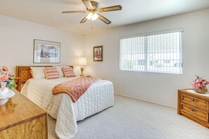 Quarto com cama, mesa de cabeceira, cômoda, ventilador de teto e janela com persianas.
