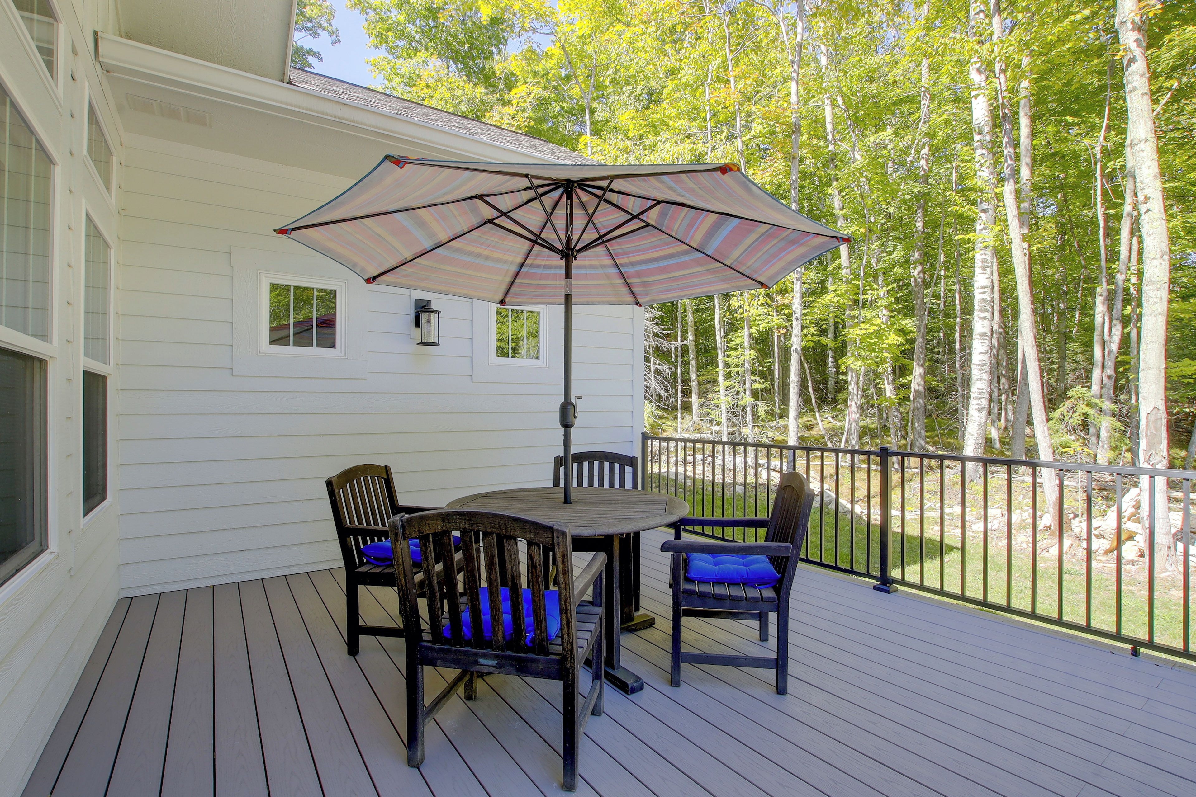 A deck with a table and chairs, a striped umbrella, and a view of trees.