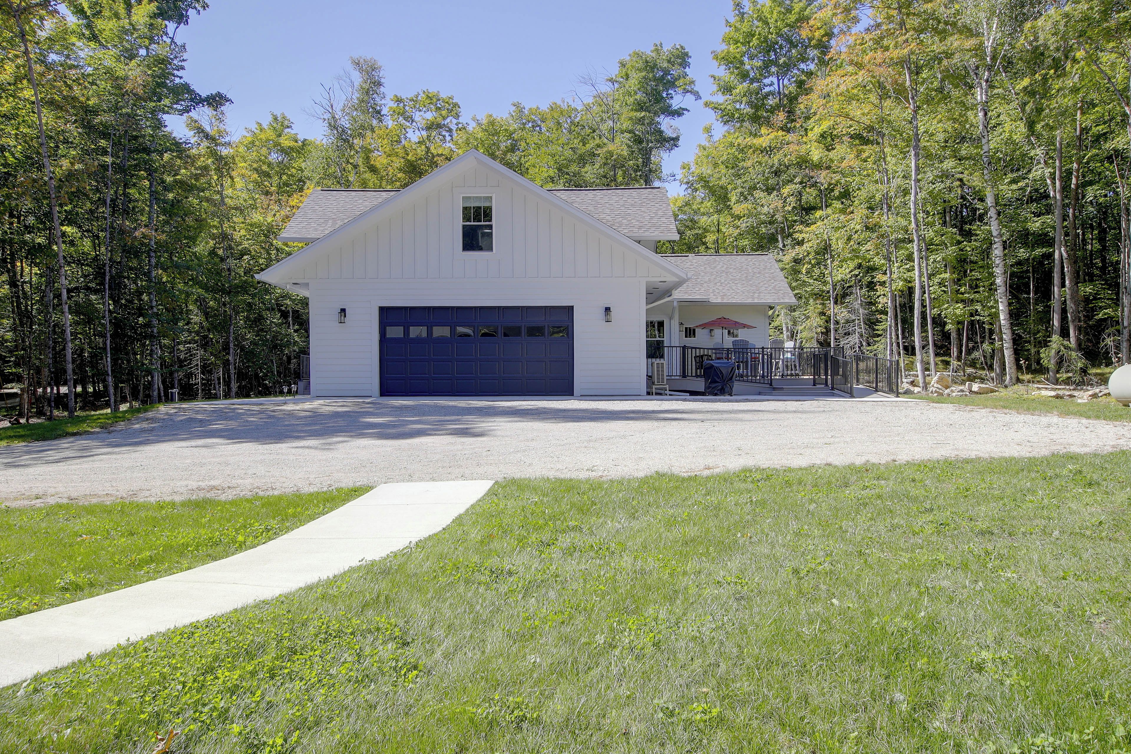 A white barn-style building with a garage, surrounded by a gravel driveway and a grassy area.