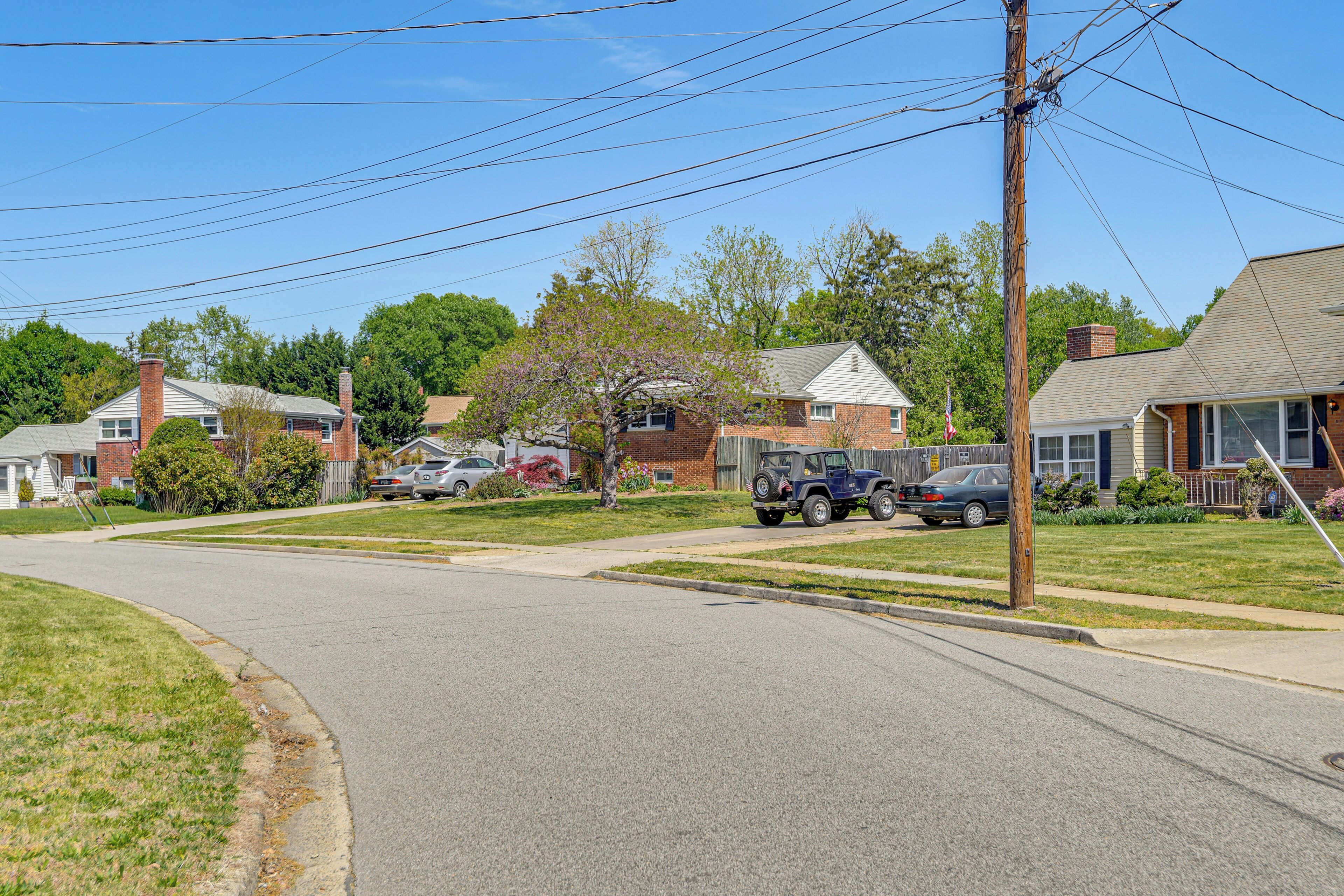 A residential street with houses, parked cars, and a clear sky.