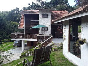 A two-story house with a balcony, a car parked outside, and a chair in the foreground. - Wooden house. (Campos do Jordão)