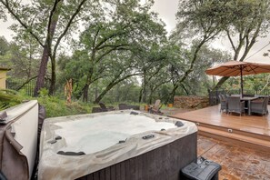 A hot tub on a wooden deck with outdoor furniture and a covered area.