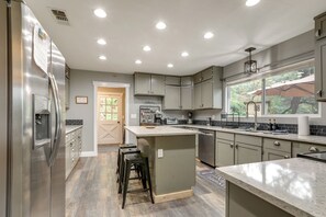 A modern kitchen with a stainless steel refrigerator, a large island, and a window with an umbrella.