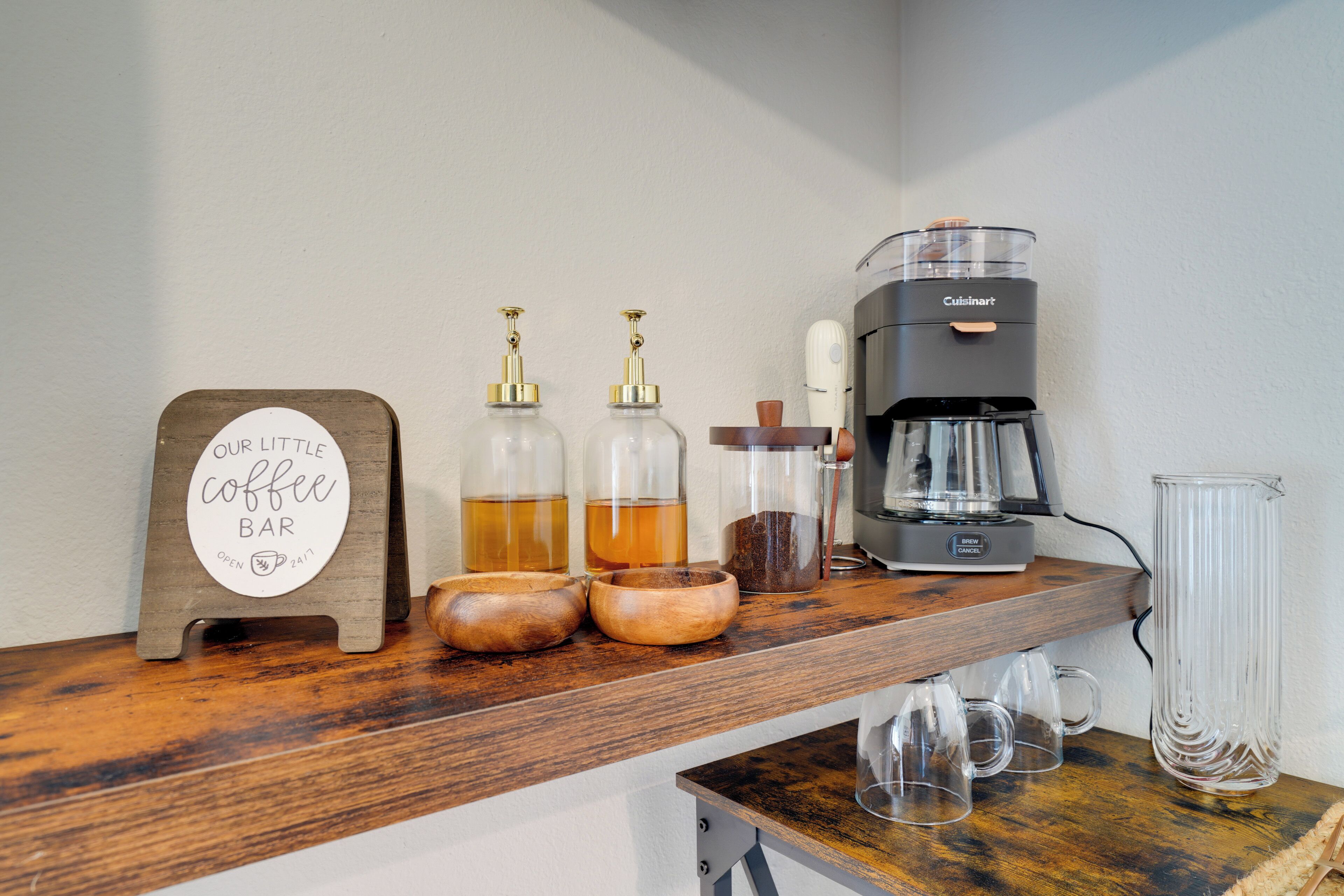 A coffee bar setup with a sign, coffee dispensers, a coffee maker, and mugs.