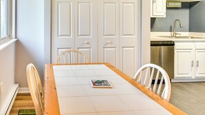 Zona pranzo con tavolo, sedie e un libro. Si intravede in lontananza una cucina con pensili e una lavastoviglie.