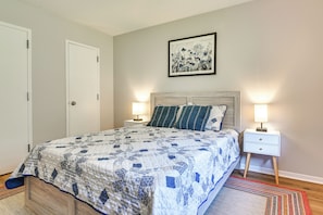 A bedroom with a bed, two bedside tables, a nightstand, a door, and a framed picture on the wall.