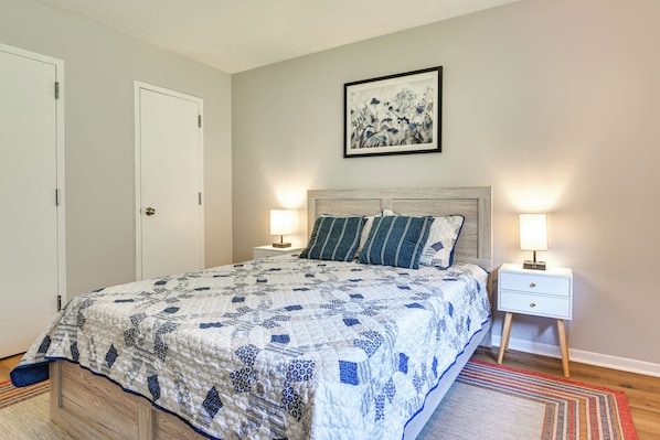 A bedroom with a bed, two bedside tables, a nightstand, a door, and a framed picture on the wall.