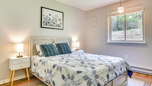 Un dormitorio con una cama, dos mesitas de noche, una lámpara de noche, una ventana con vistas y un aplique de techo.
