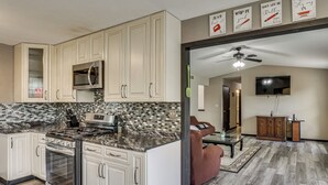 A kitchen with white cabinets, a microwave, and a stove. There is a living area with a couch and a TV.