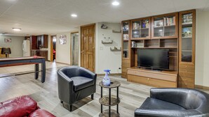 A living room with a pool table, leather chairs, a TV, and a bookshelf.
