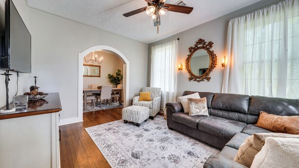 A living room with a ceiling fan, a television, a sofa, an ottoman, and a dining area with a chandelier. - Private Deck & Yard: Pet-friendly Noble Getaway (Noble)
