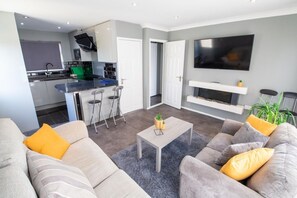 A modern living room with a grey sofa, a coffee table, and a TV mounted on the wall. - Yew 2 Bungalow, Parkdean Resorts - Camber Sands (Camber)