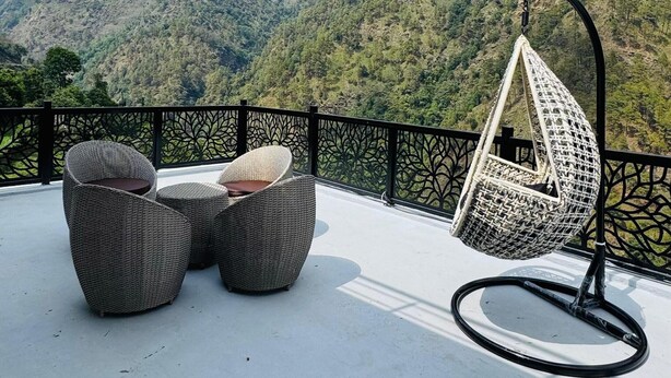 A balcony with wicker furniture and a hanging chair overlooking a mountainous landscape. - Hotel Shri Hari And Restaurant (Ukhimath)