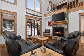 Amplia sala de estar con sofás de cuero, chimenea, televisor y balcón.
