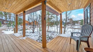 Une terrasse en bois dotée d’un espace abrité, d’une chaise et offrant une vue sur un paysage enneigé, avec des arbres et des maisons.