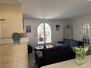 A living room with a fireplace, a sofa, a dining table with chairs, and a view through a large arched window.