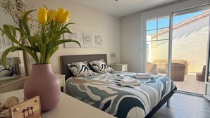 Un dormitorio con cama, una mesita de noche, una lámpara, un jarrón con flores y vistas al exterior.