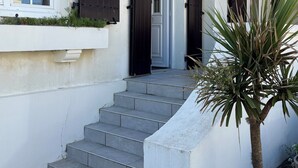 Un edificio con fachada blanca, un conjunto de escalones grises que llevan a una puerta, y una palmera pequeña en primer plano.