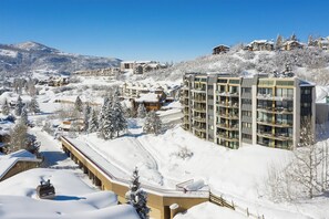 Ein schneebedecktes Bergresort mit mehrstöckigen Gebäuden, darunter ein Hotel mit Balkonen und eine Seilbahn.