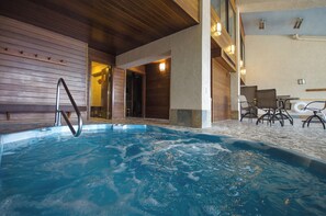 Ein Innenpool mit Holzwänden und Steinboden, umgeben von Sitzgelegenheiten und einer Treppe.