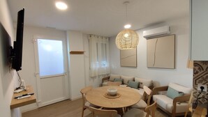Un espace repas comprenant une table ronde, des chaises, un luminaire suspendu, un canapé et un téléviseur fixé au mur.