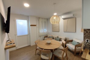 Ein Essbereich mit einem runden Tisch, Stühlen, einer Hängelampe, einer Couch und einem an der Wand befestigten Fernseher.