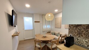 Un espace de vie compact comprenant une table à manger, des chaises, un canapé, une machine à café et un téléviseur fixé au mur.