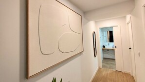Un couloir orné d’un grand tableau abstrait, une porte donnant sur une salle de bain et une vue sur une pièce où se trouve un lavabo.