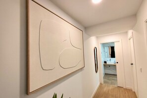 Ein Flur mit einem großen abstrakten Gemälde, einer zur Toilette führenden Tür und Blick in einen Raum mit einem Waschbecken.