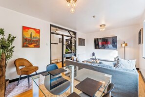 Ein modernes Wohnzimmer mit einem Glastisch, einer Couch, einem Fernseher und einem Gemälde an der Wand.