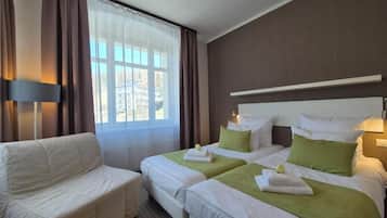 A hotel room with two beds, a sofa, a large window, and a lamp.