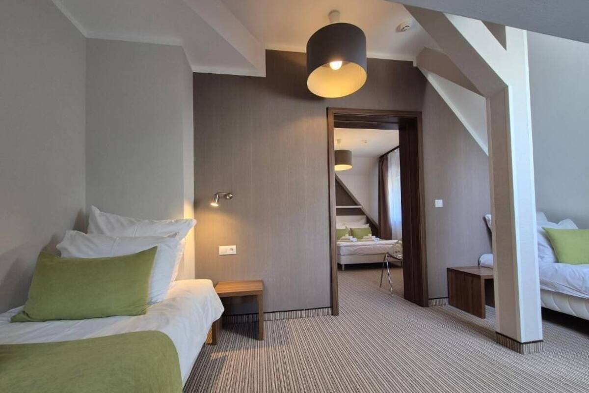 Quarto de hotel com cama, um banco, escrivaninha, luminária e escada que dá para outro cômodo.