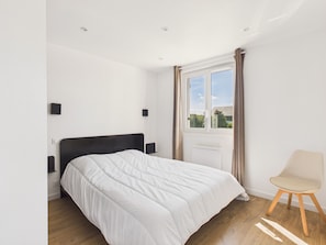 Une chambre à coucher avec un lit, une chaise, une fenêtre avec des rideaux et une vue sur la verdure à l’extérieur.