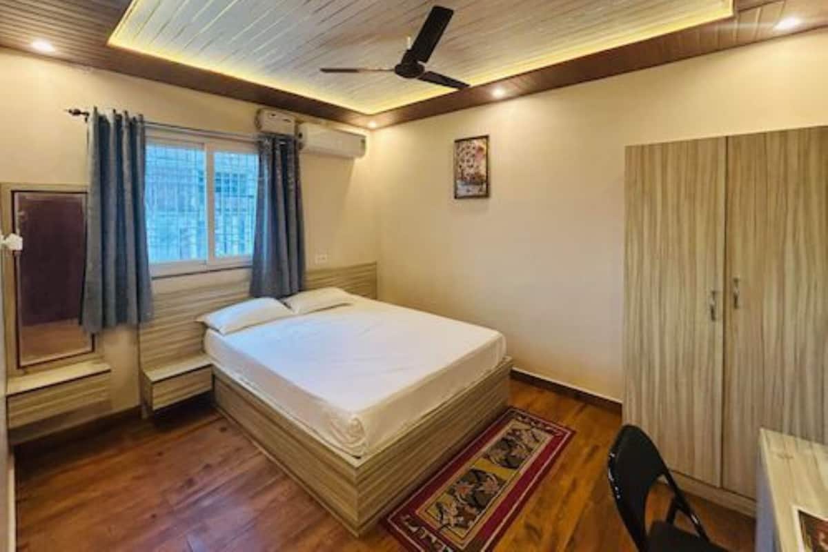 A bedroom with a bed, a ceiling fan, a window with curtains, a wardrobe, and a desk with a chair.