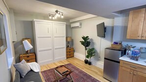 Un salon comprenant un canapé, une table basse, un téléviseur, une cuisine avec un réfrigérateur et une armoire.