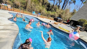 Piscina rodeada de árboles y un área cercada con sillas de descanso.