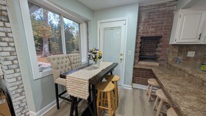 Una cocina con pared de ladrillo, una mesa de comedor con taburetes y vistas a árboles a través de una ventana.