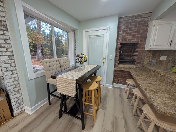 A kitchen with a brick wall, a dining table with stools, and a view of trees through a window.