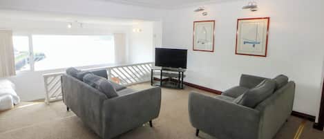 A modern living room with two grey sofas, a flat-screen TV, and framed nautical artwork on the walls.